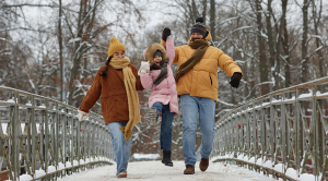 Full length portrait of happy family with daughter jumping up and holding hands while walking towards camera on bridge in winter